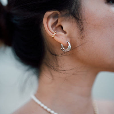 Close-up of a person wearing gold and silver hoop earrings with a blurred background.